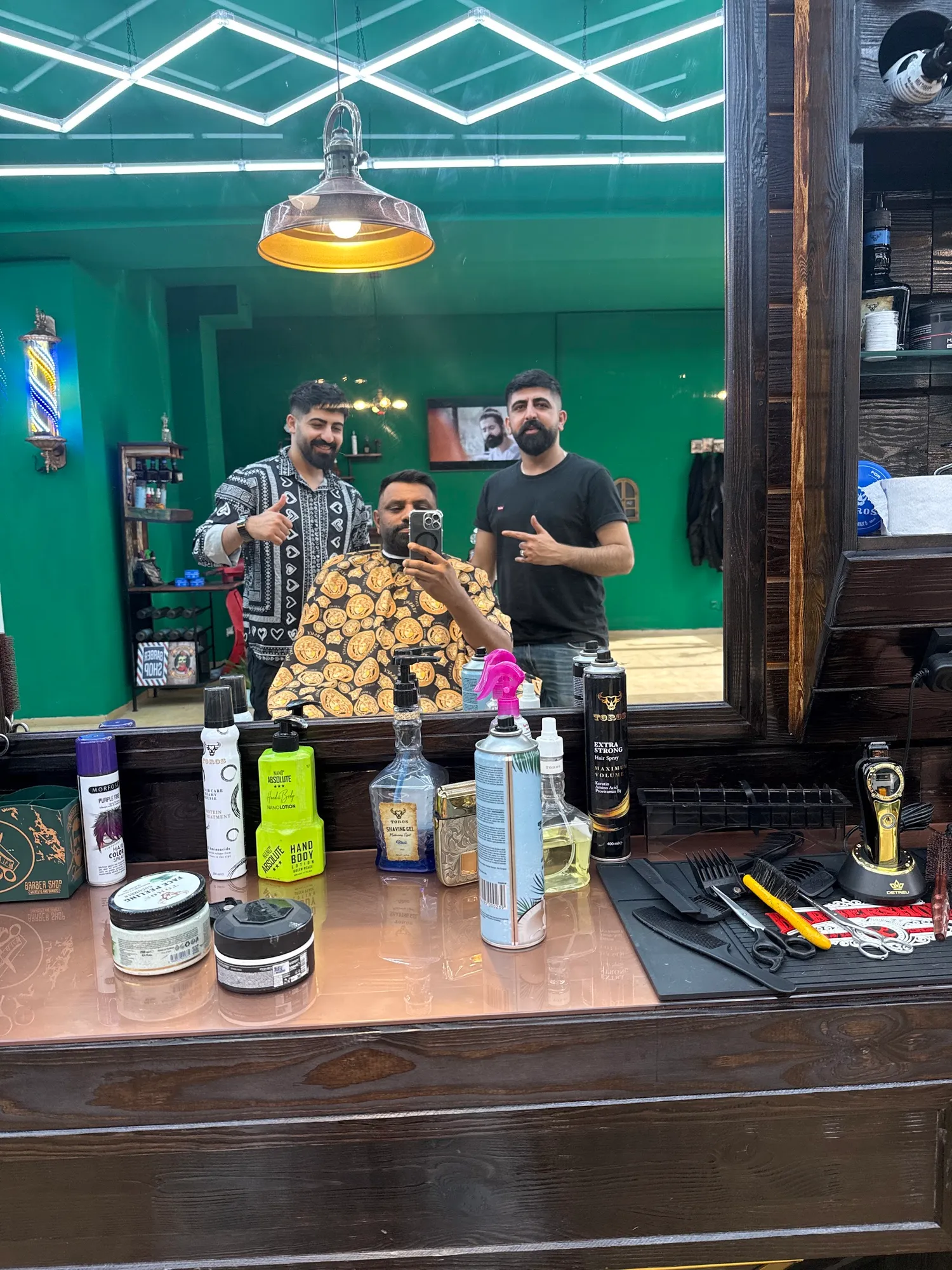 Blick in den Spiegel bei Ari Barbershop: grüne Wände, Neonlicht an der Decke, zwei Barbiere und ein Kunde im Stuhl
